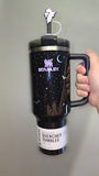 Black Stanley tumbler with a handle held by a hand on a gray background