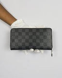 Black wallet with a pattern held by a hand wearing a white glove on a light gray background