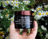Hand holding a jar of Fresh Black Tea Firming Corset Cream against a floral background