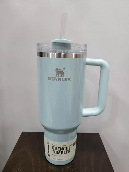 Light blue Stanley tumbler with handle on a wooden surface and light gray background
