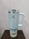 Light blue Stanley tumbler with handle on a wooden surface and light gray background