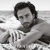 Man lying on a log by the water with 'Acqua di Gio' branding.