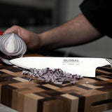 Person using a Global brand knife to chop an onion on a wooden cutting board.
