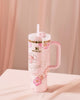 Pink tumbler with floral design and handle on a light pink background