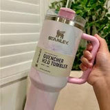 Stanley tumbler with pink handle held by a person against a white background