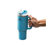 Turquoise Stanley mug with handle held by a hand on a white background